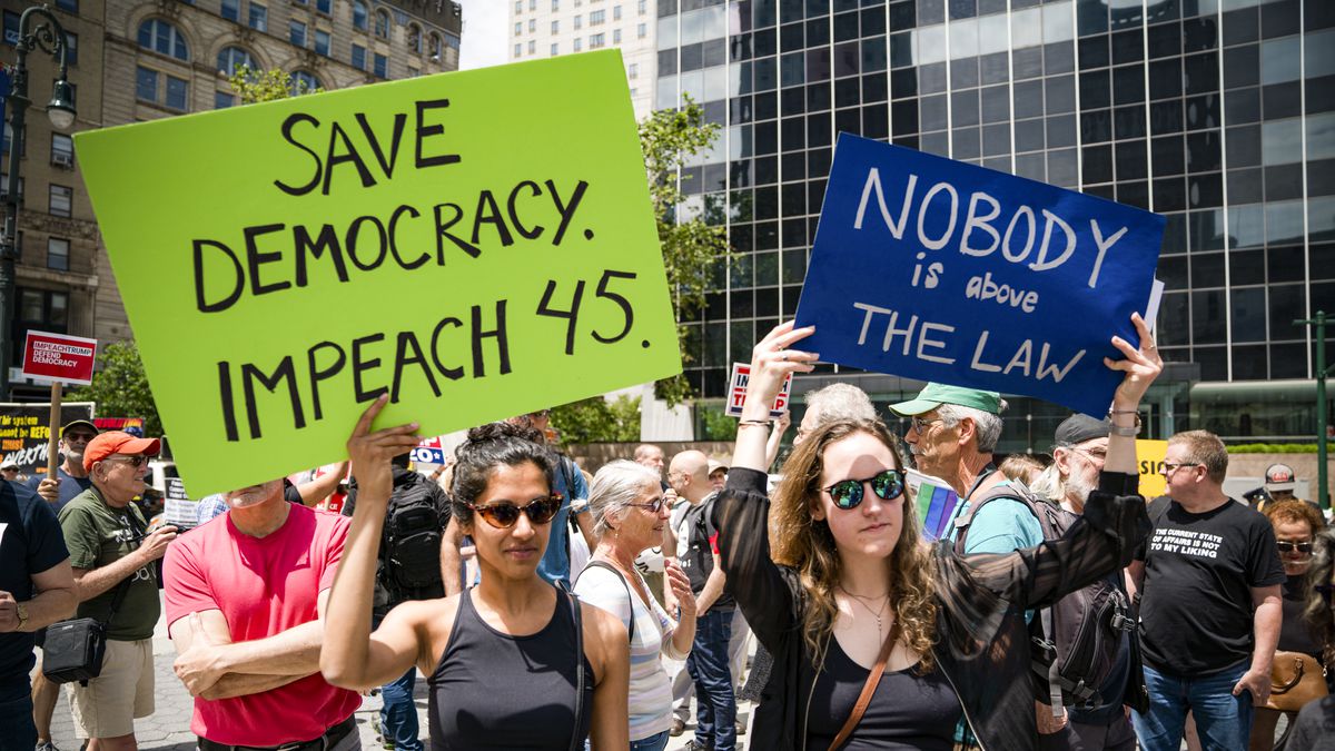 Protesters call for the impeachment of President Trump during a demonstration. One holds a sign that reads, “Save democracy. Impeach 45.” Another reads, “Nobody is above the law.”