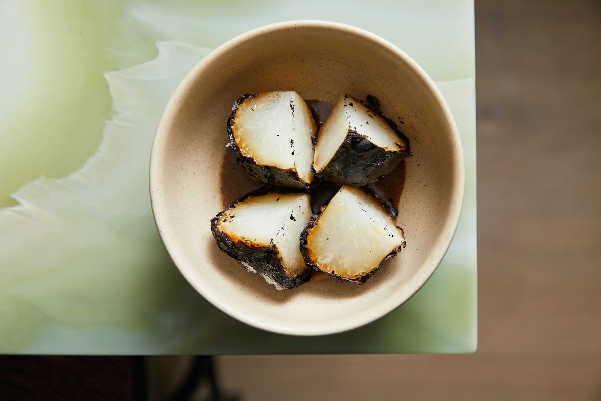 A whole kohlrabi with dark, burnt looking exterior is divided into four pieces and served in a bowl.