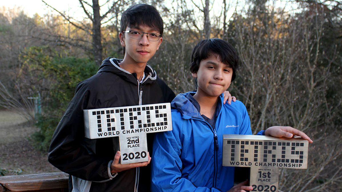 A 15-year-old boy standing next to a 13-year-old boy. Each of them is holding a statue for 2020’s Classic Tetris World Championship.