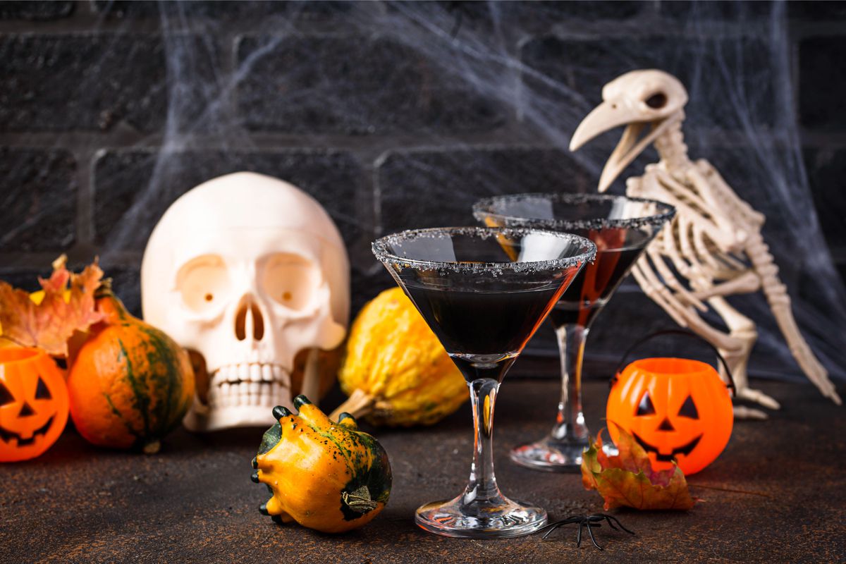A Halloween display, with plastic jack o’ lanterns, gourds, a bird skeleton, a skull, and two martini glasses filled with a dark liquid.