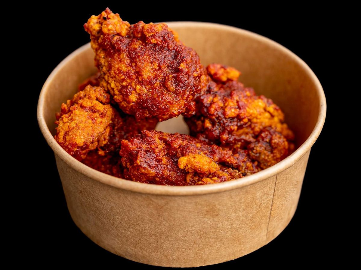 A takeout container filled with pieces of fried chicken against a black background.