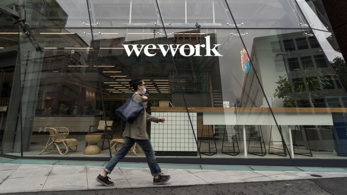 A man wearing a mask walks in front of a WeWork building.