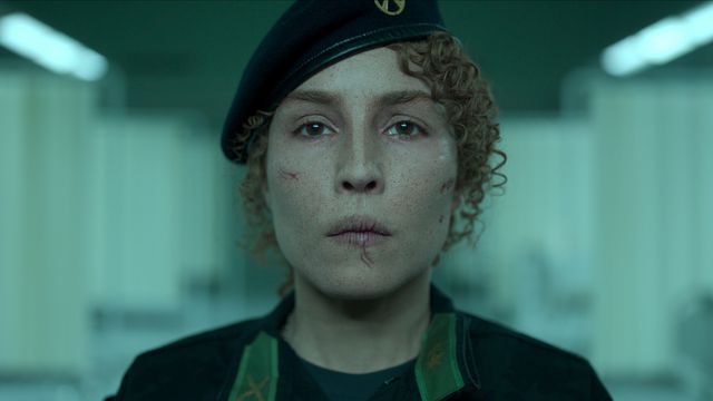 Noomi Rapace wears a military uniform and look straight ahead in Black Crab. Her face is bruised and cut.