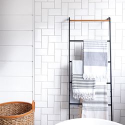 Painted shiplap tempers the hard “clink” of tile in the tub alcove. A ladder-style towel rack adds a welcome vertical element to the room.