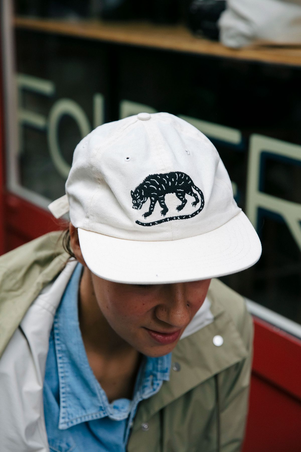 A woman seated shows off her white baseball cap with tiger embroidery.