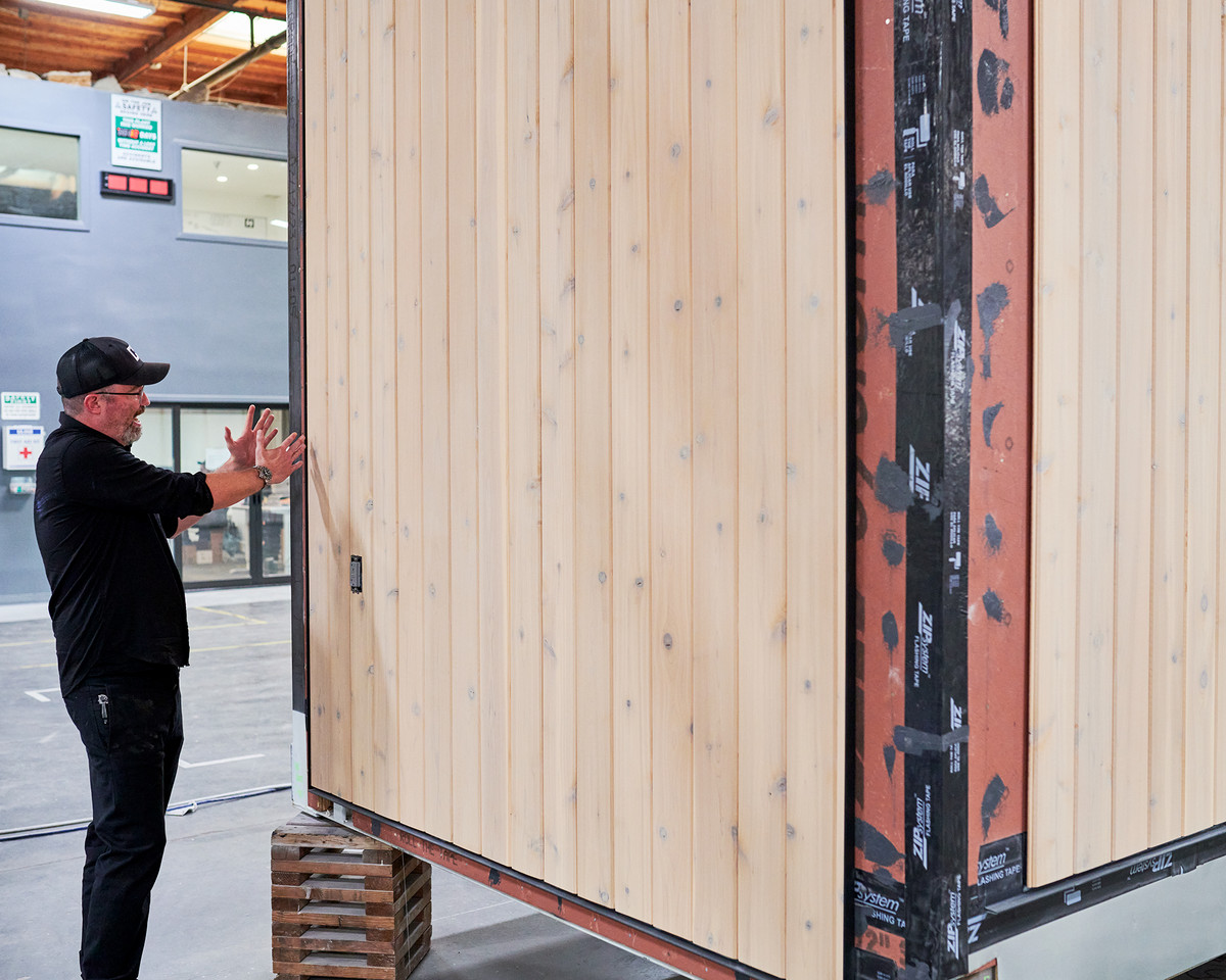 A worker talks next to a partly finished wooden tiny house being built inside a factory.