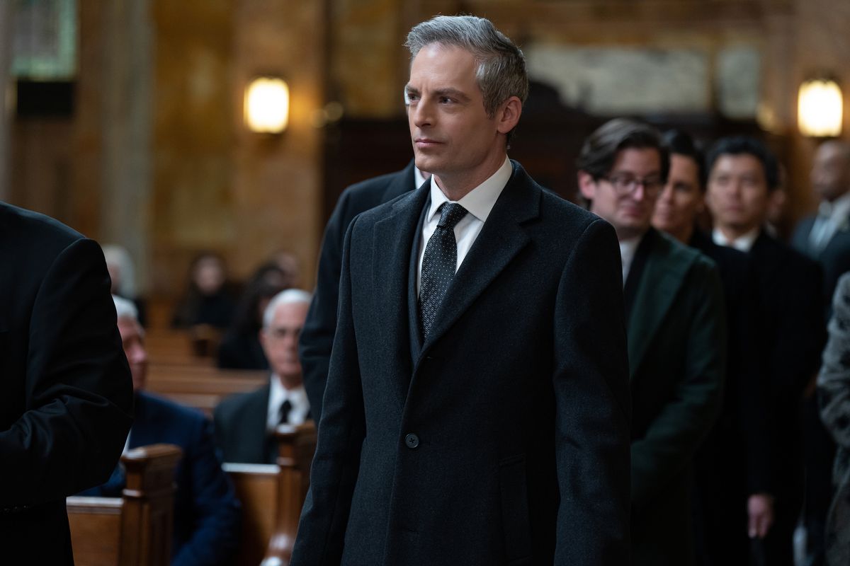 Actor Justin Kirk, as presidential candidate Jeryd Mencken, wears a black suit and attends a church service, with people seated in pews shown behind him.