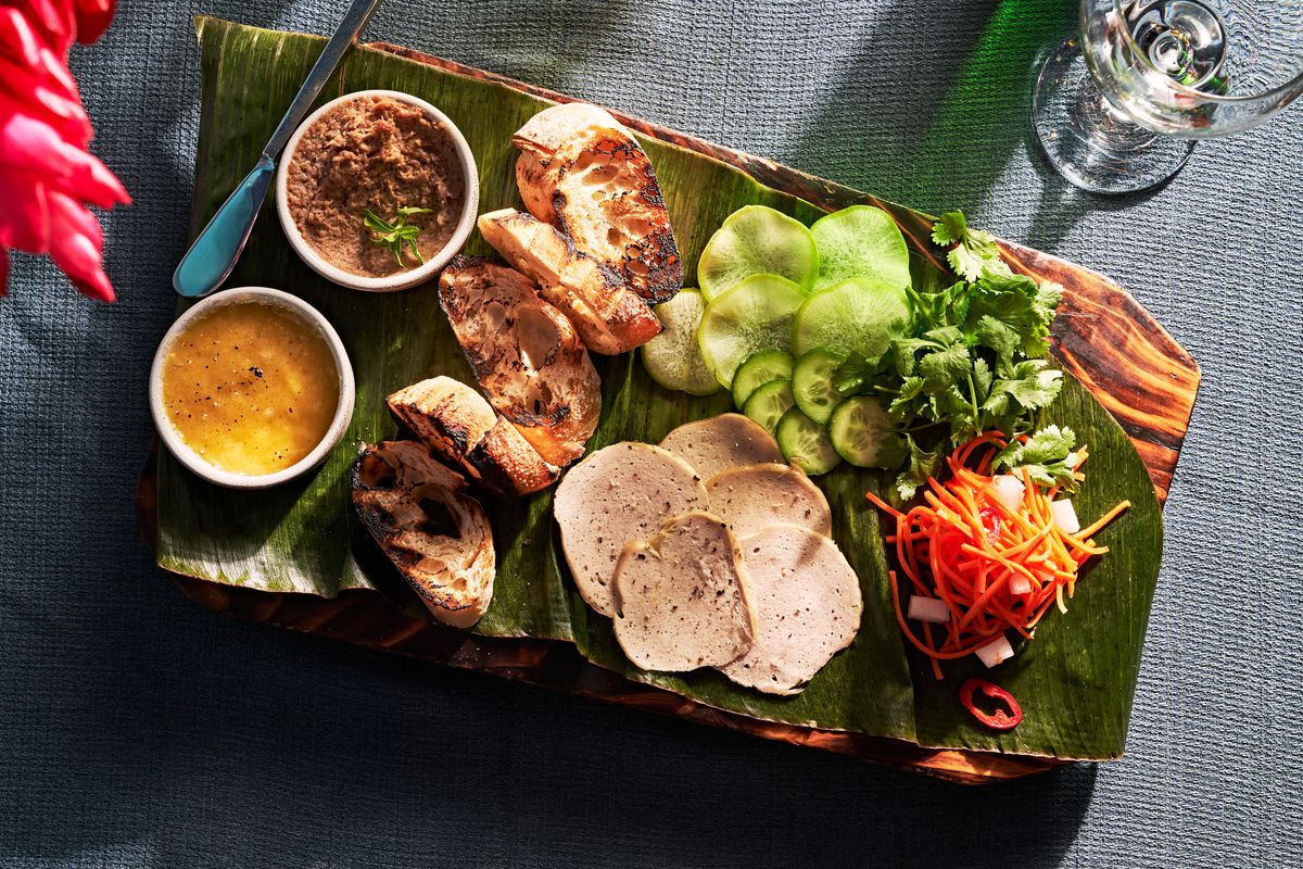A wooden board with a green leaf spread over top and deconstructed banh mi ingredients laid out.