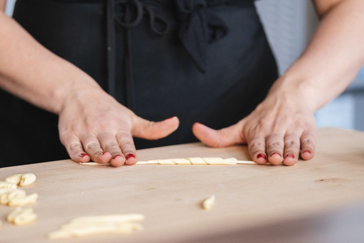 Hands twist pasta around a wooden spool.