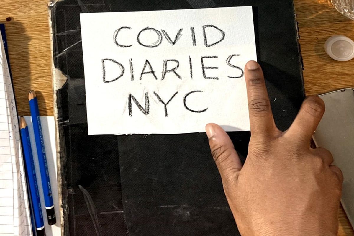 A hand rests on a black-covered book with lettering that says “Covid Diaries NYC.”