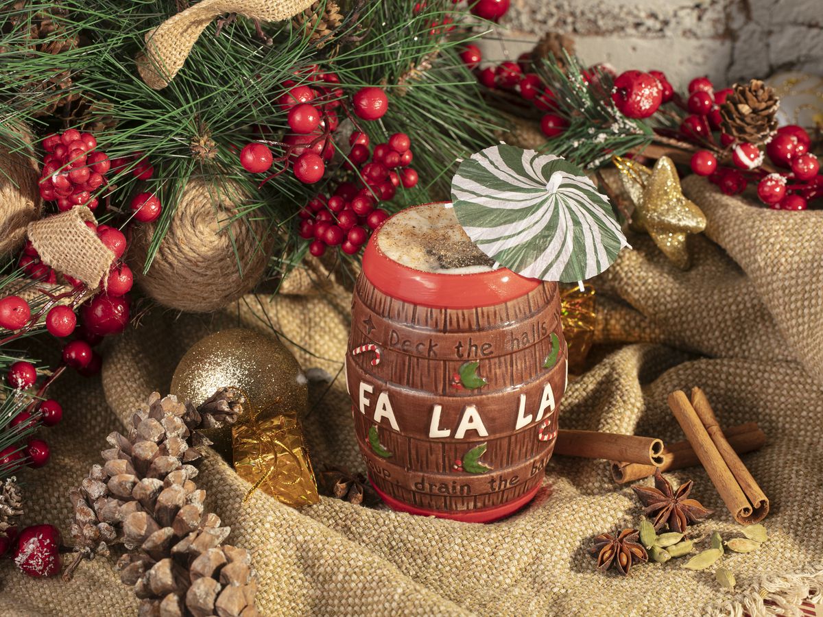A mug engraved with the words “Fa La la” appears in a festive background with pinecones, cinnamon, and carnberries.