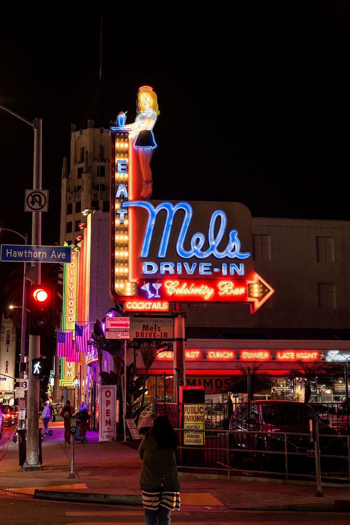 A tall neon sign showing parking lot entry into a vintage diner, at night.