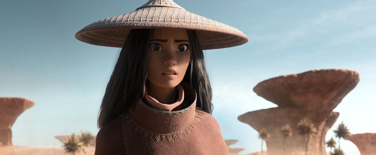 Raya from Raya and the Last Dragon, in a woven brown sun-hat and brown cloak, looks toward the horizon with a worried face 