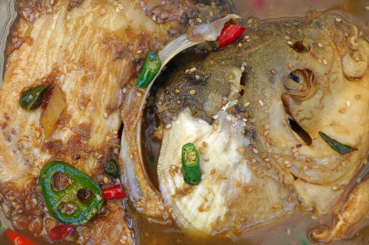 A squished gray fish head littered with red and green chiles.