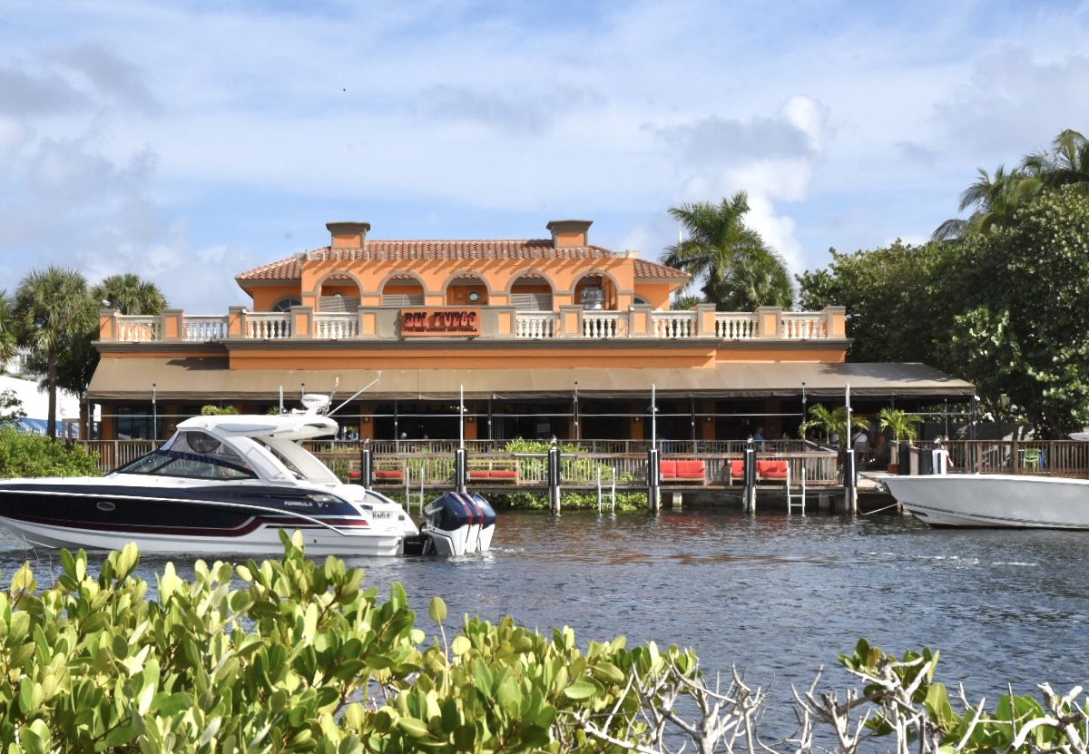 This is a picture of Del Fuego restaurant. It’s a dark terracotta color. The intracoastal waterway is in front of the restaurant. Boats are in the water. 