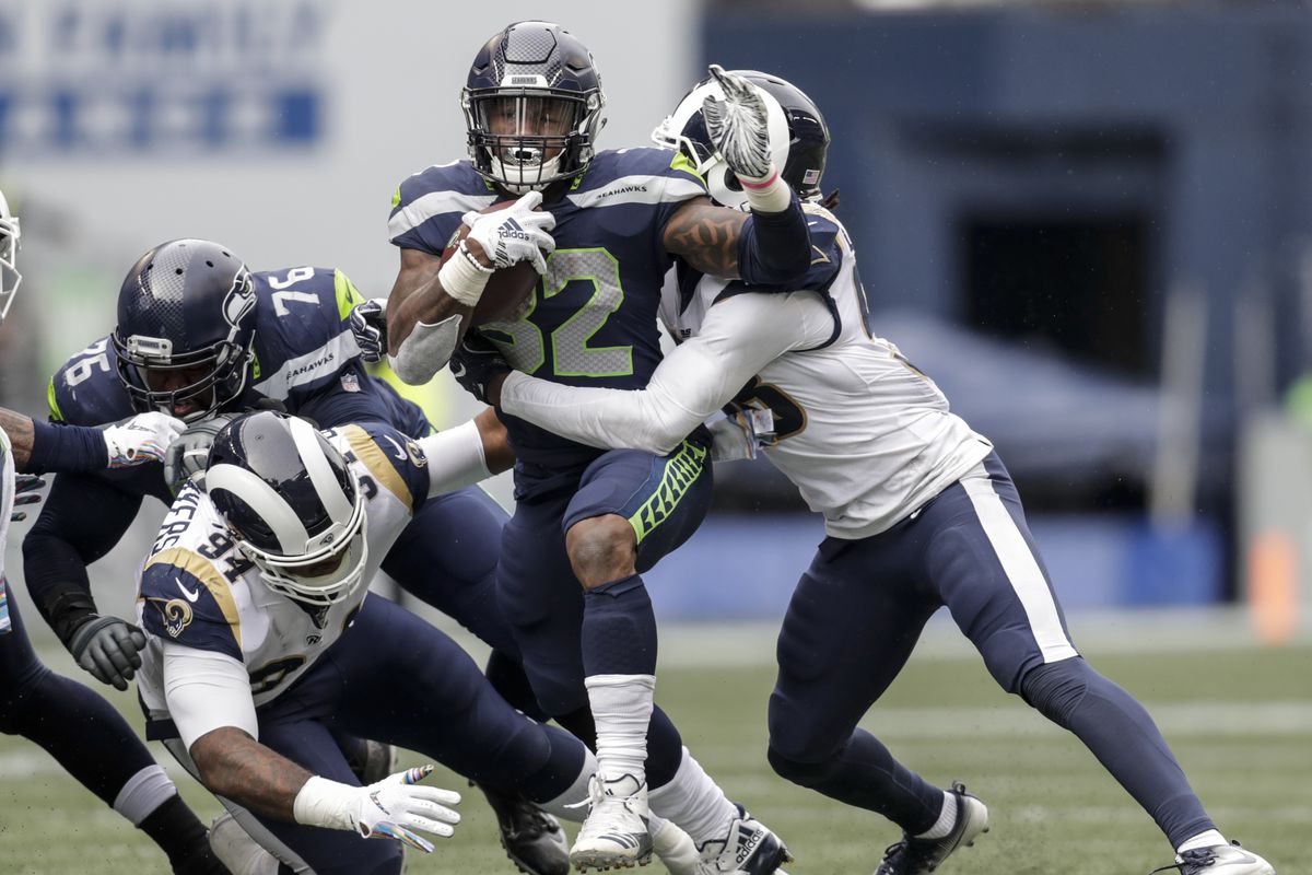 Seattle Seahawks running back Chris Carson runs with the ball as Los Angeles Rams defensive end John Franklin-Myers and linebacker Cory Littleton make a tackle during a game at CenturyLink Field on October 7, 2018 in Seattle, Washington.