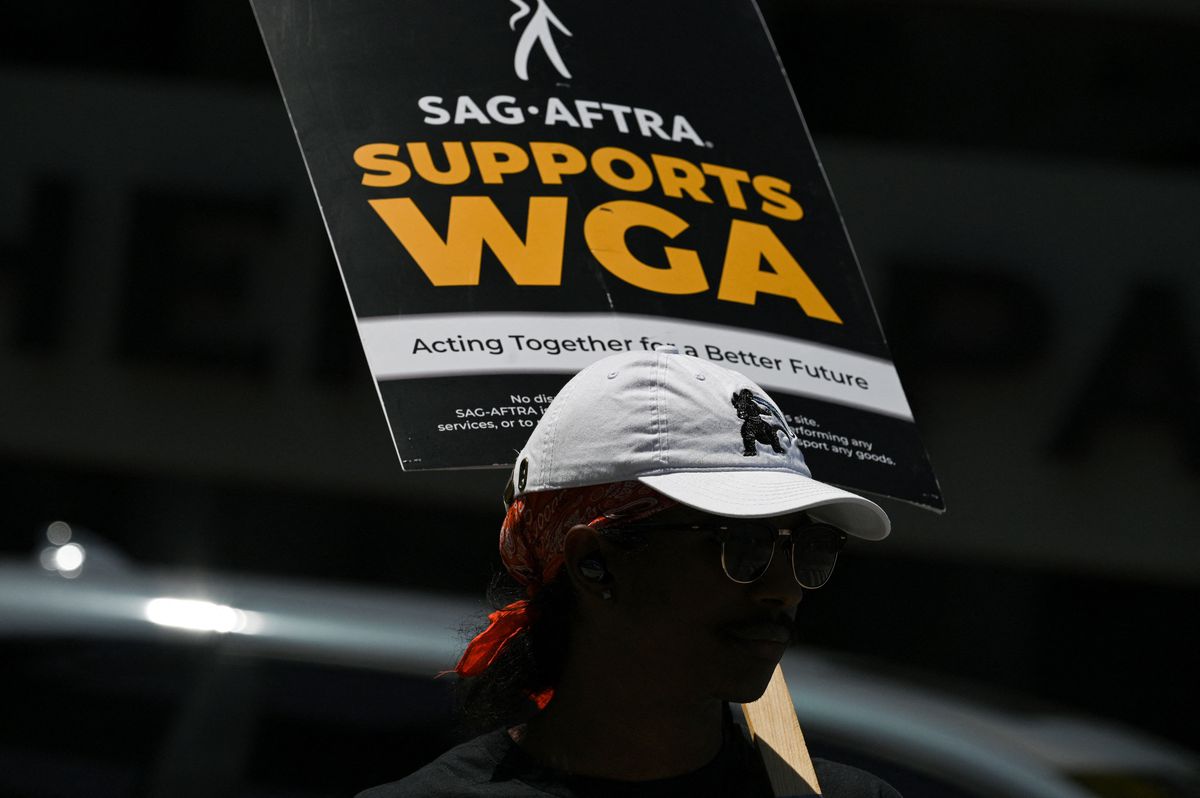 A picketer in a baseball cap carries a sign that reads “SAG-AFTRA supports WGA.”
