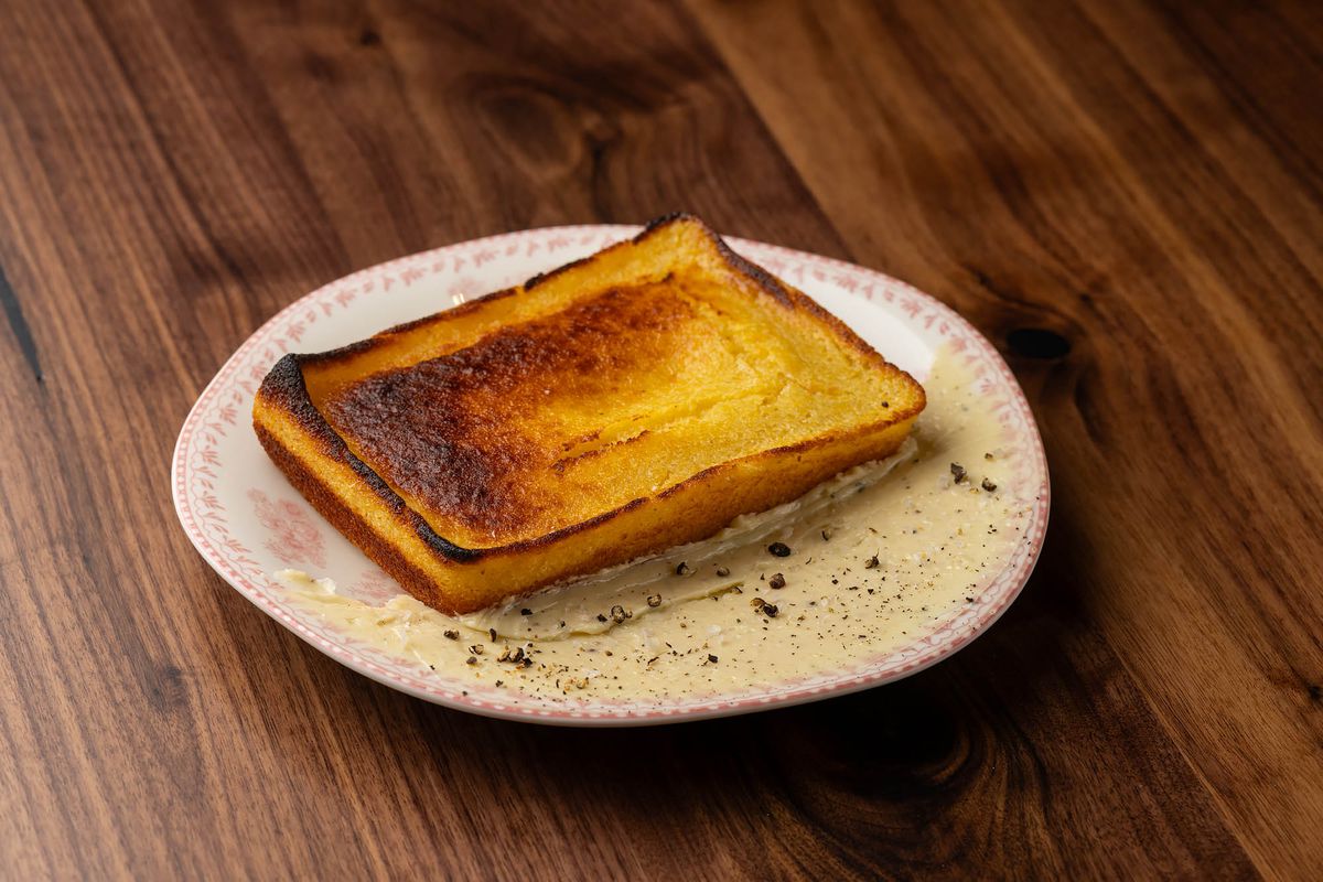 A toasted square of orange-yellow cornbread on a white and pink plate against a wooden table at new restaurant Joyce.