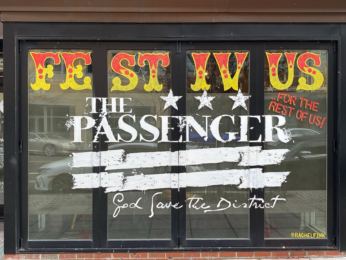 the exterior plate-glass window of The Passenger Bar painted with red and yellow Festivus lettering saying “Festivus for the rest of us! The Passenger. God save the district.”