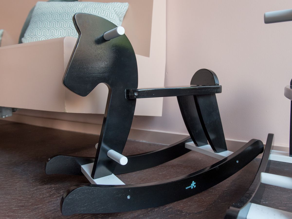 A closeup of a black rocking horse next to a pink booth.