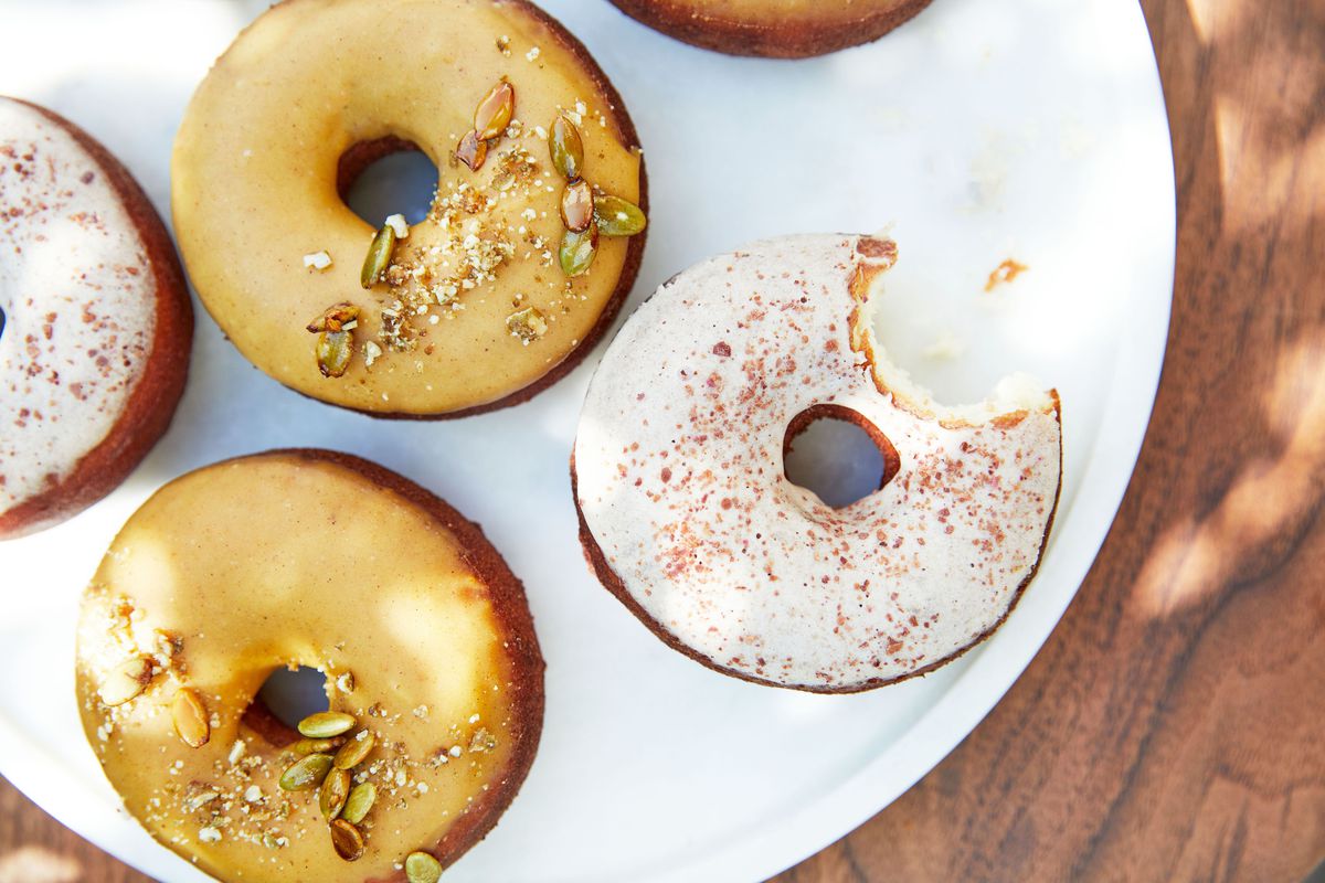 An overhead look at gluten-free doughnuts on a round white plate and wooden table in the sun.