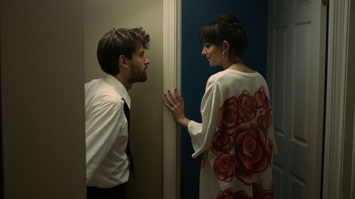 Andrew (Cooper Raiff) approaches Domino (Dakota Johnson) in a beige hallway in Cha Cha Real Smooth