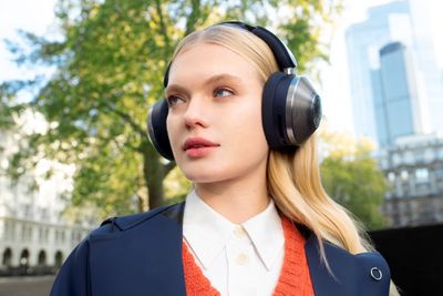 A woman outside against a city backdrop wearing the Dyson Zone headphones without the detachable visor.