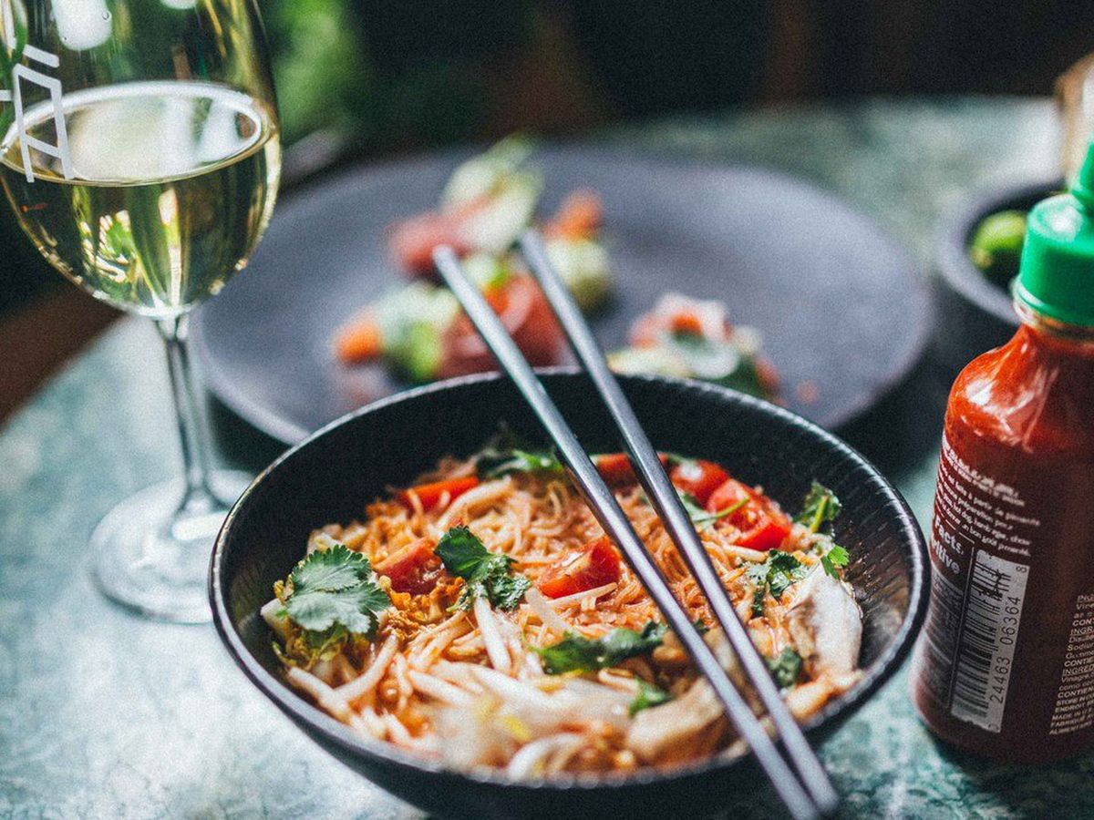 A bowl of Vietnamese soup next to a glass of wine on a table.