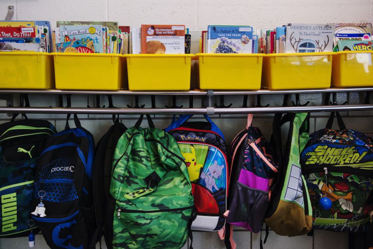 Backpacks hang from hooks in a classroom.