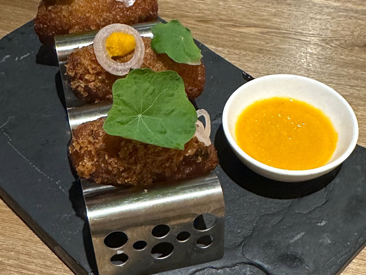 Fried croquettes presented in a small metal holder with dipping sauce.