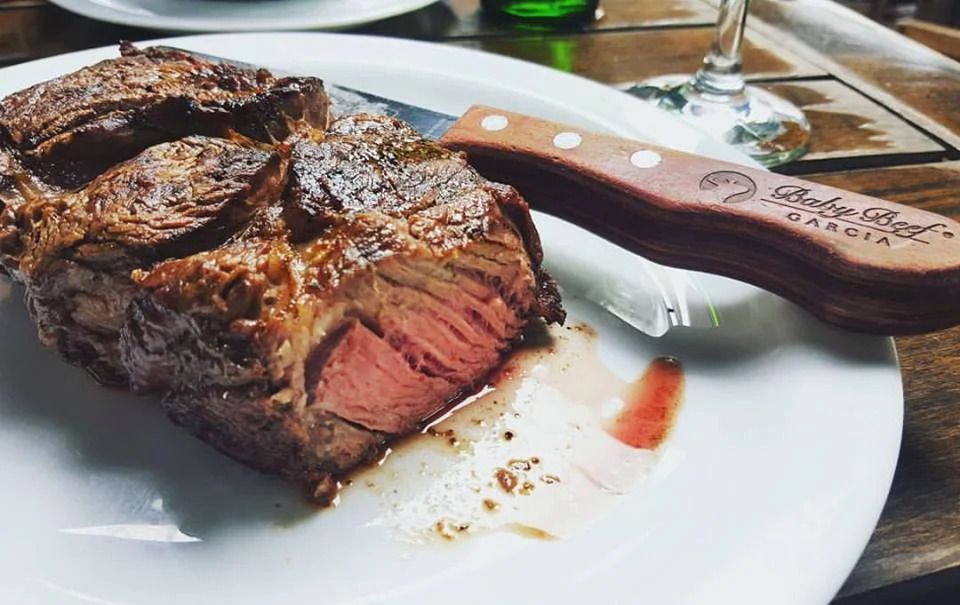 A closeup on a hunk of steak sliced to reveal its red center, next to a branded steak knife.