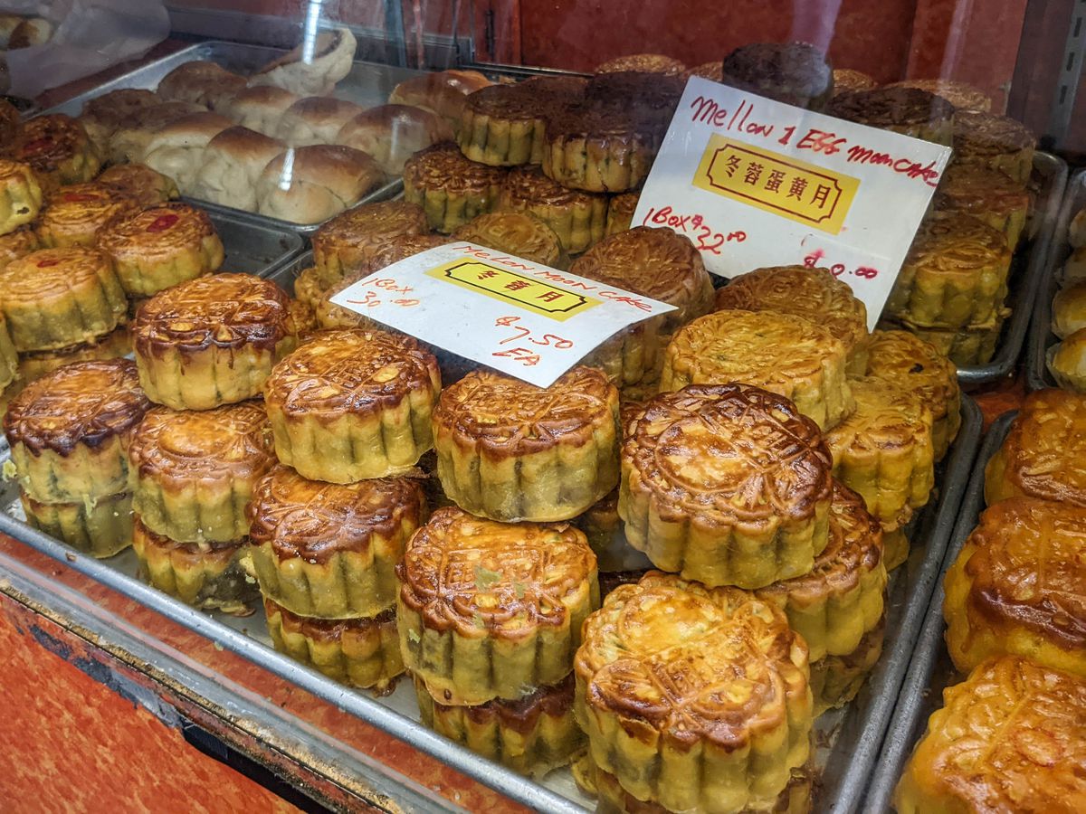 Round mooncakes with a scalloped edge and golden-brown crust are displayed on metal trays in a pastry case.