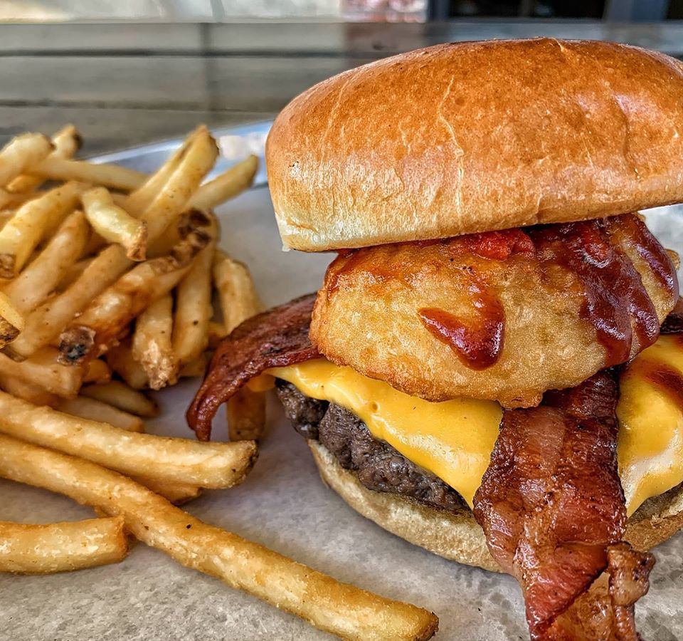 A burger stacked with an onion ring and bacon, available for ordering at the Bar Code Burger Bar.