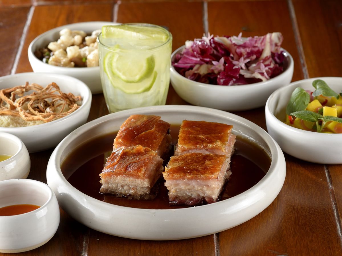 A plate of four large hunks of roasted pork meat, alongside salads and drinks.
