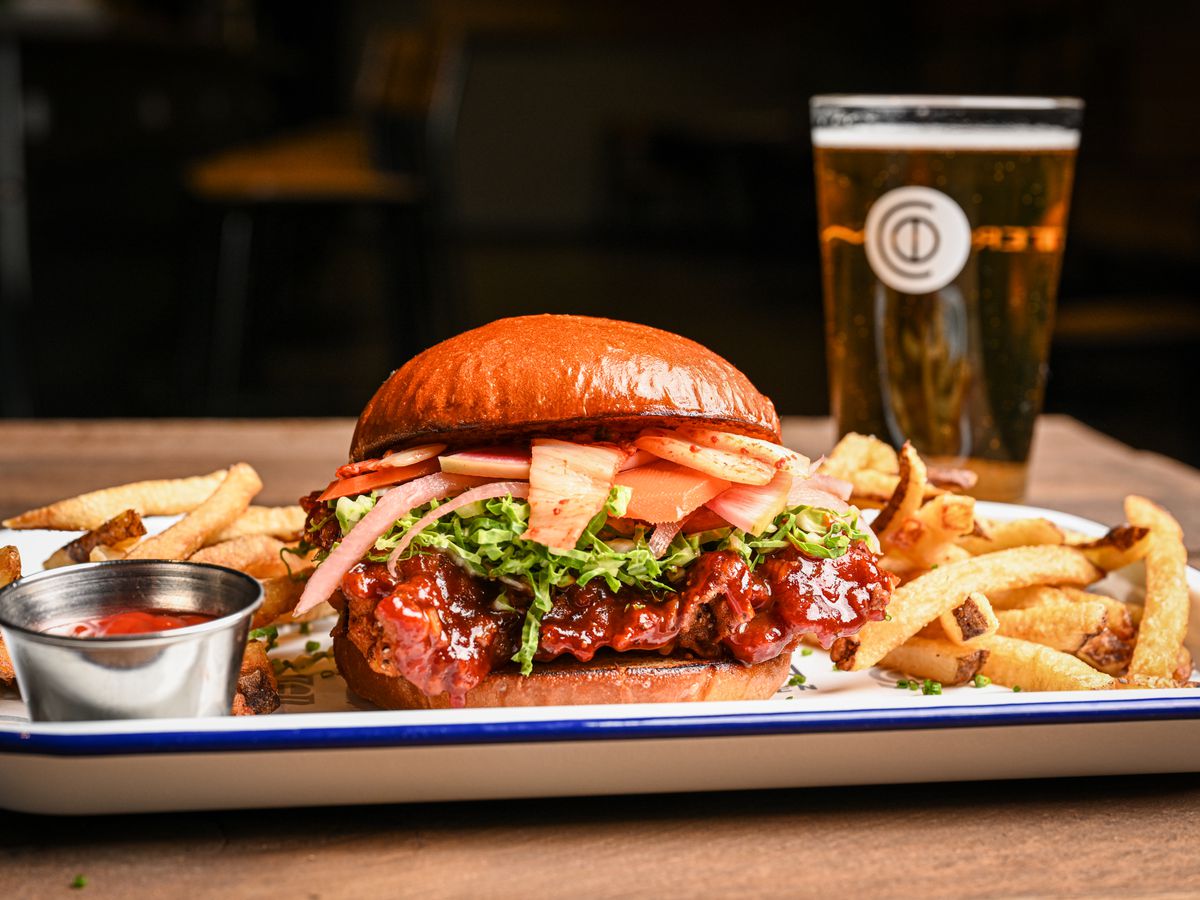 CounterCommon’s Korean fried chicken sandwich loaded with kimchi, served with a side of fries and a glass of beer.