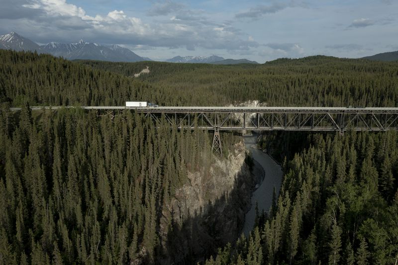 A truck drives across a bridge going over a canyon river with lots of trees.