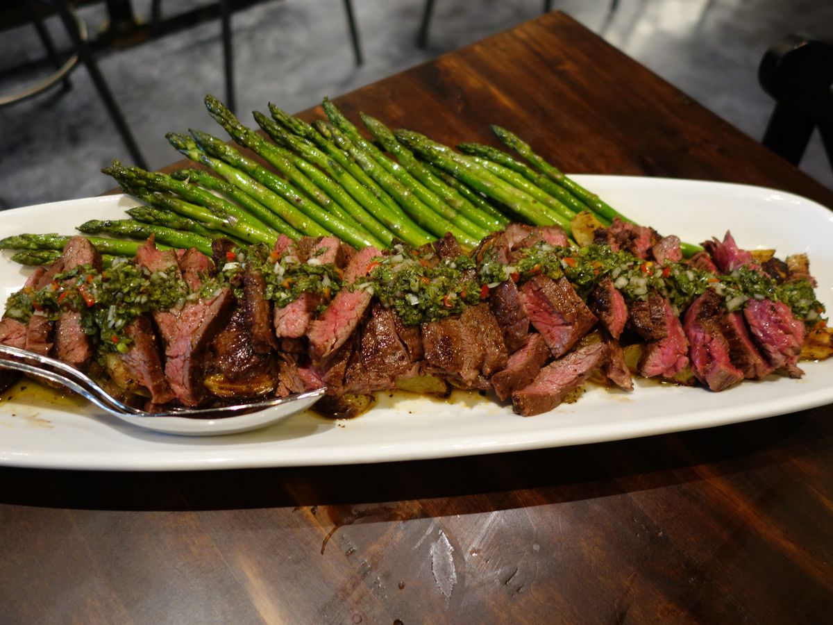 A large steak cut into slices and topped with chimichurri, served with green beans.