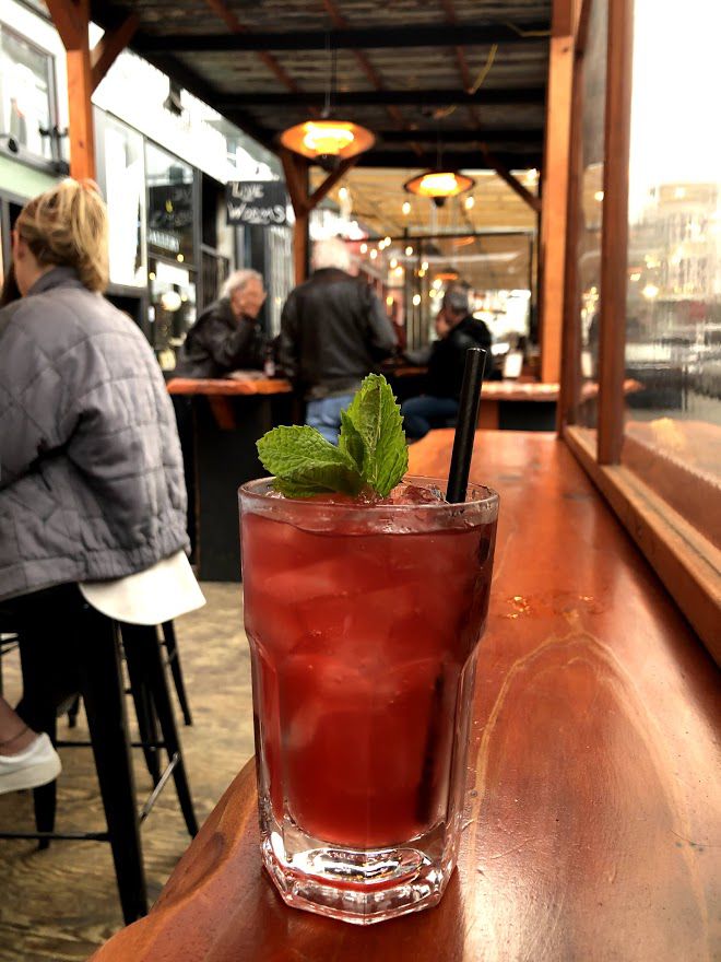 A red cocktail topped with mint and ice in an outdoor parklet