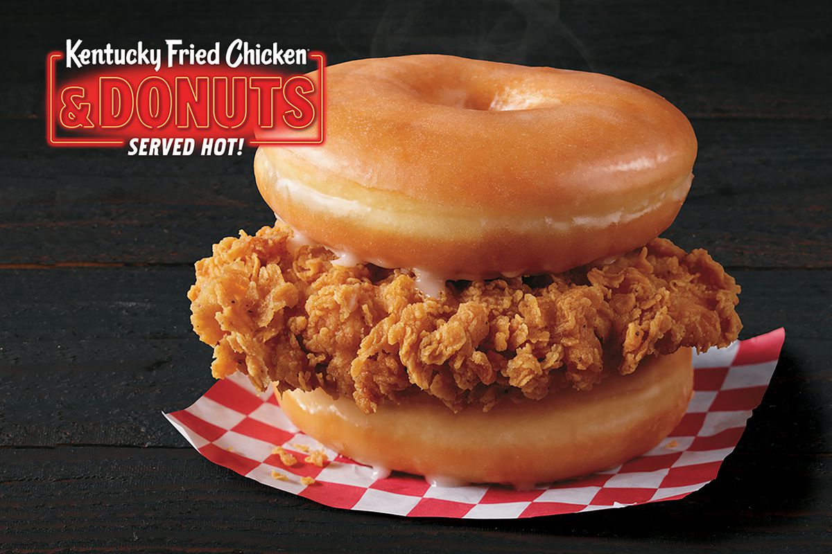 A fried chicken filet between two doughnuts on a red-and-white checkered piece of paper.