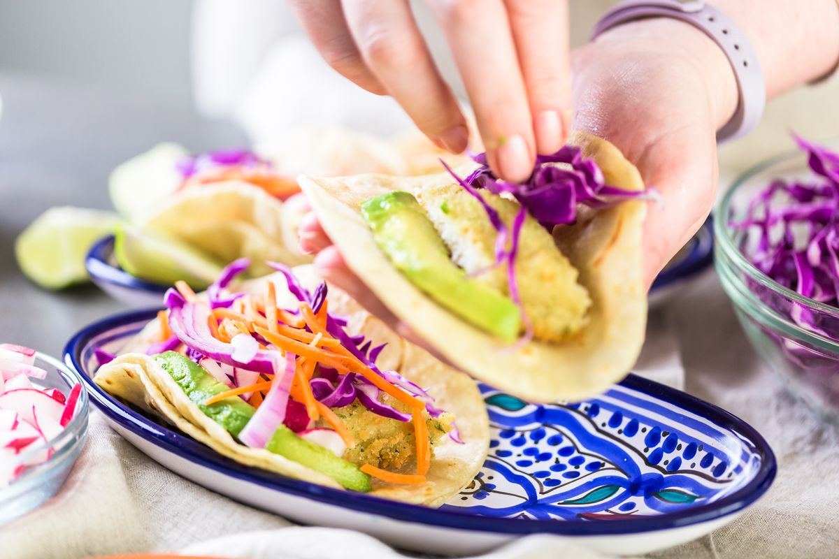 Women adds cabbage to the top of a fish taco.