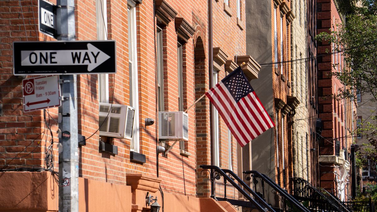 An American flag on a front porch is shown in front of row of brownstones on a New York street.