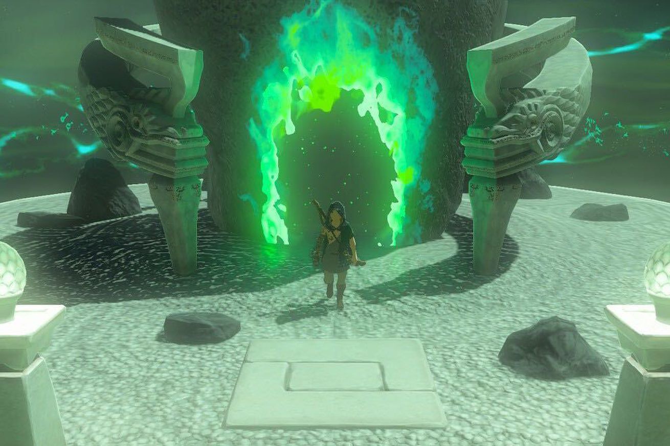 A hooded man stepping out of a glowing hole in the side of an ovular stone. The doorway in the stone is flanked by stone serpent heads, and the ground beneath the man is covered in manicured sand.