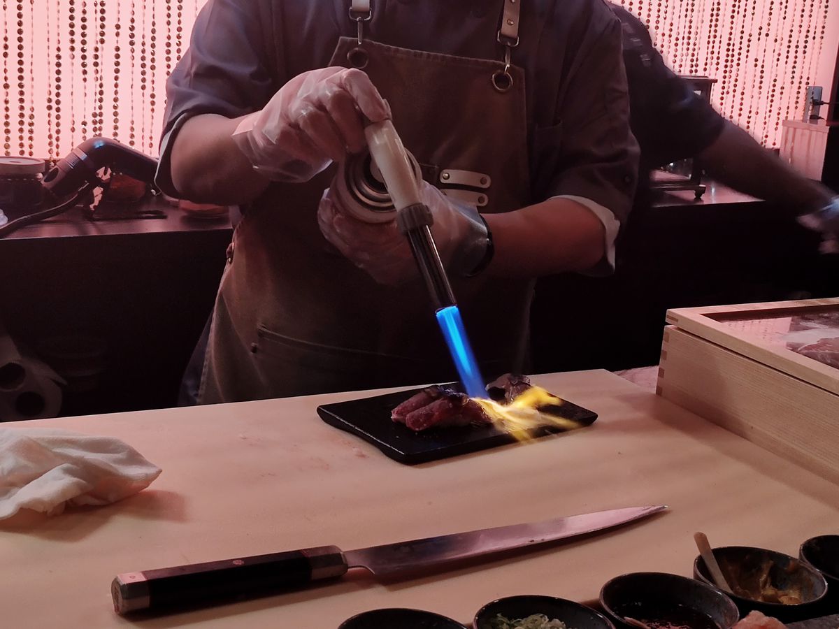 A chef is blow-torching a piece of sushi. 