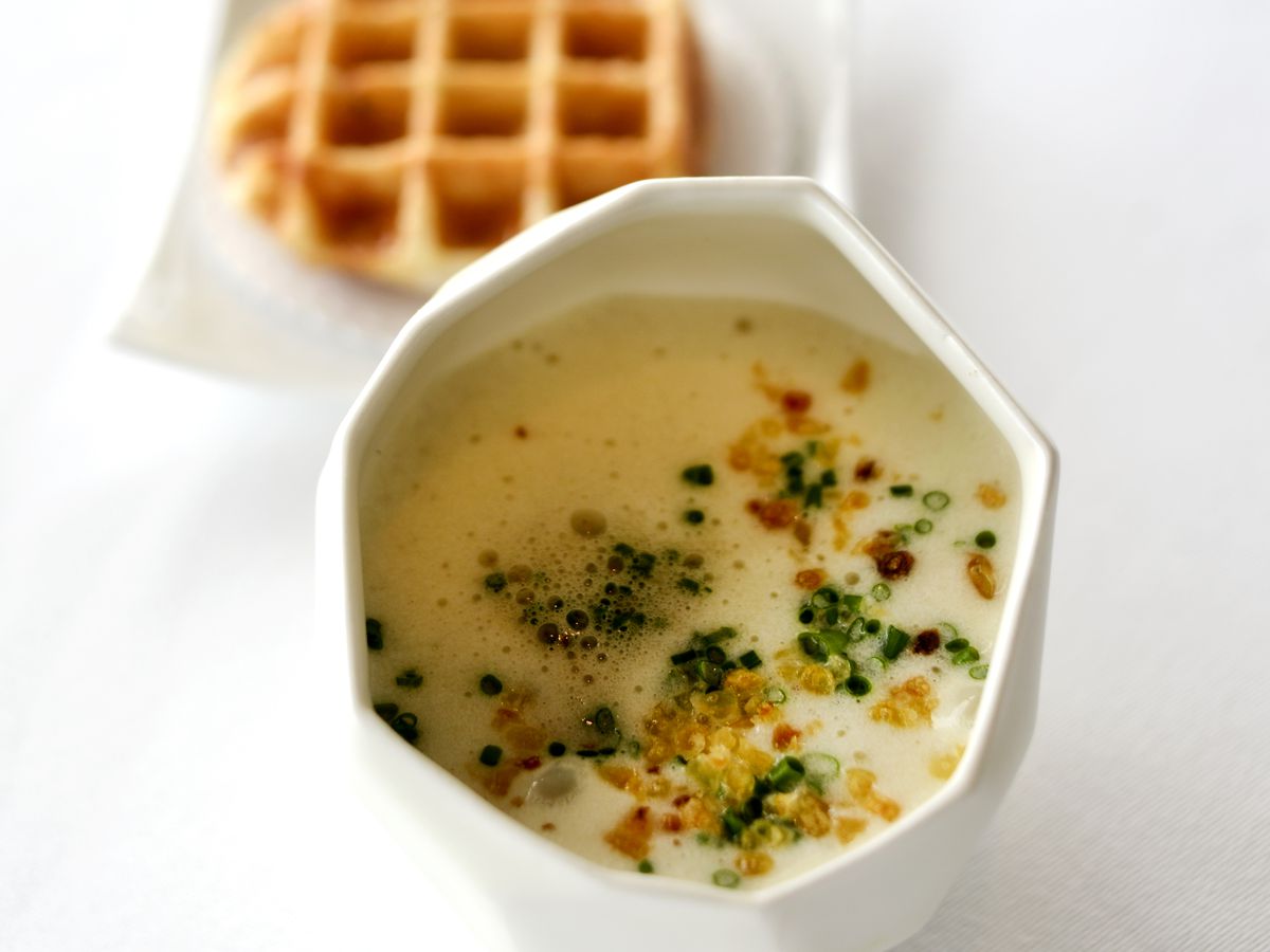A cup of soup served with a waffle.
