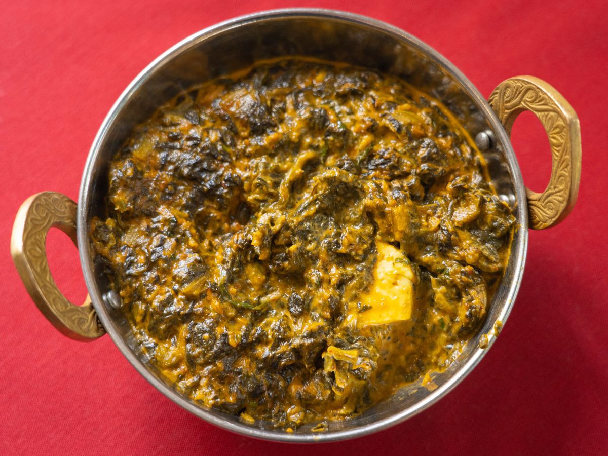 A metal bowl with handles containing spinach cooked in spices
