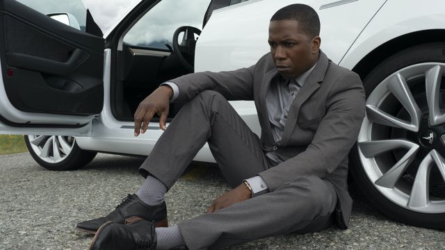 Leslie Odom Jr., in a nice grey suit, sits on the ground in front of his expensive-looking car and gets real pouty in Needle in a Timestack