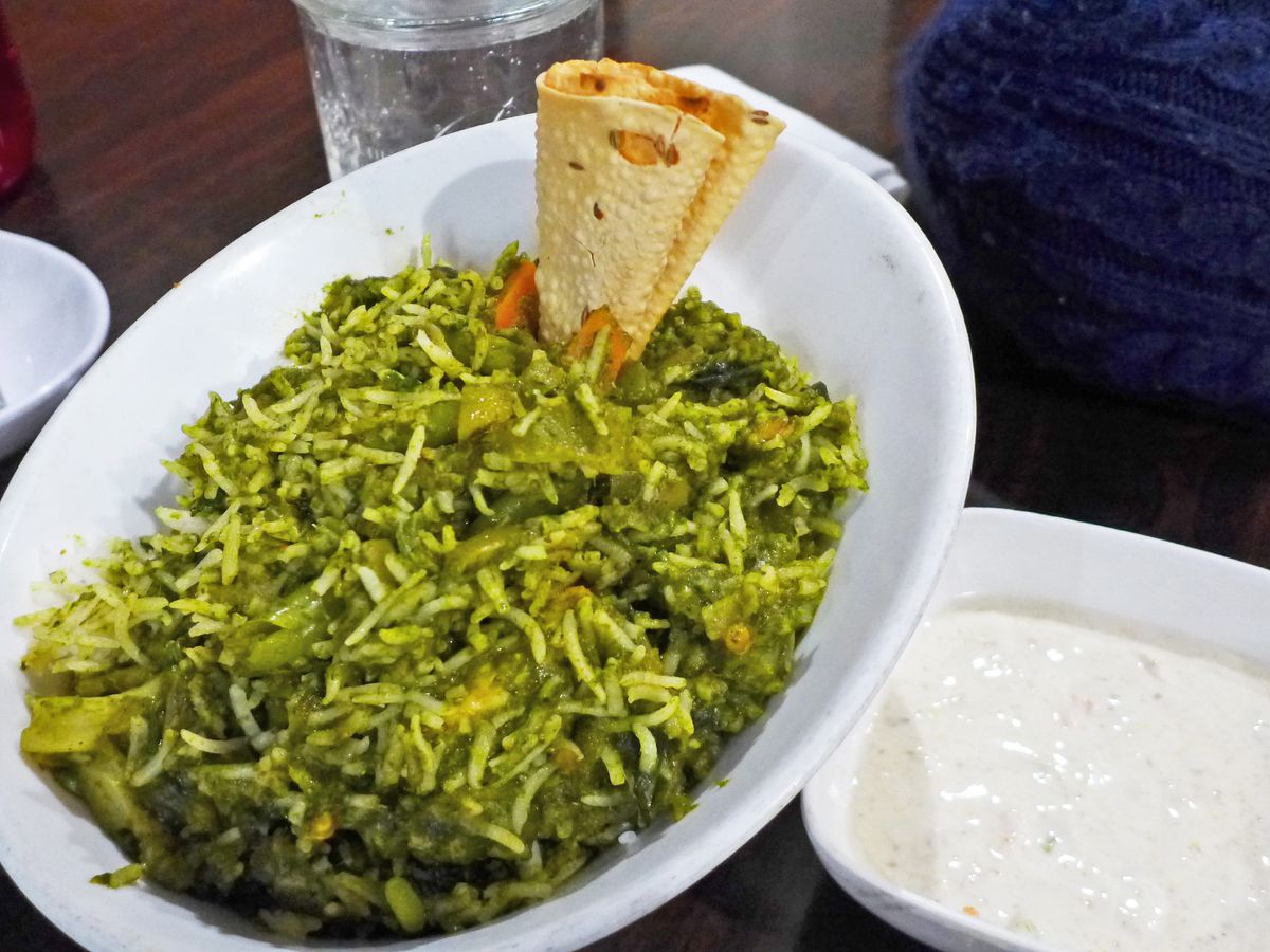 An oblong white bowl of rice and spinach, with a papadum sticking out.