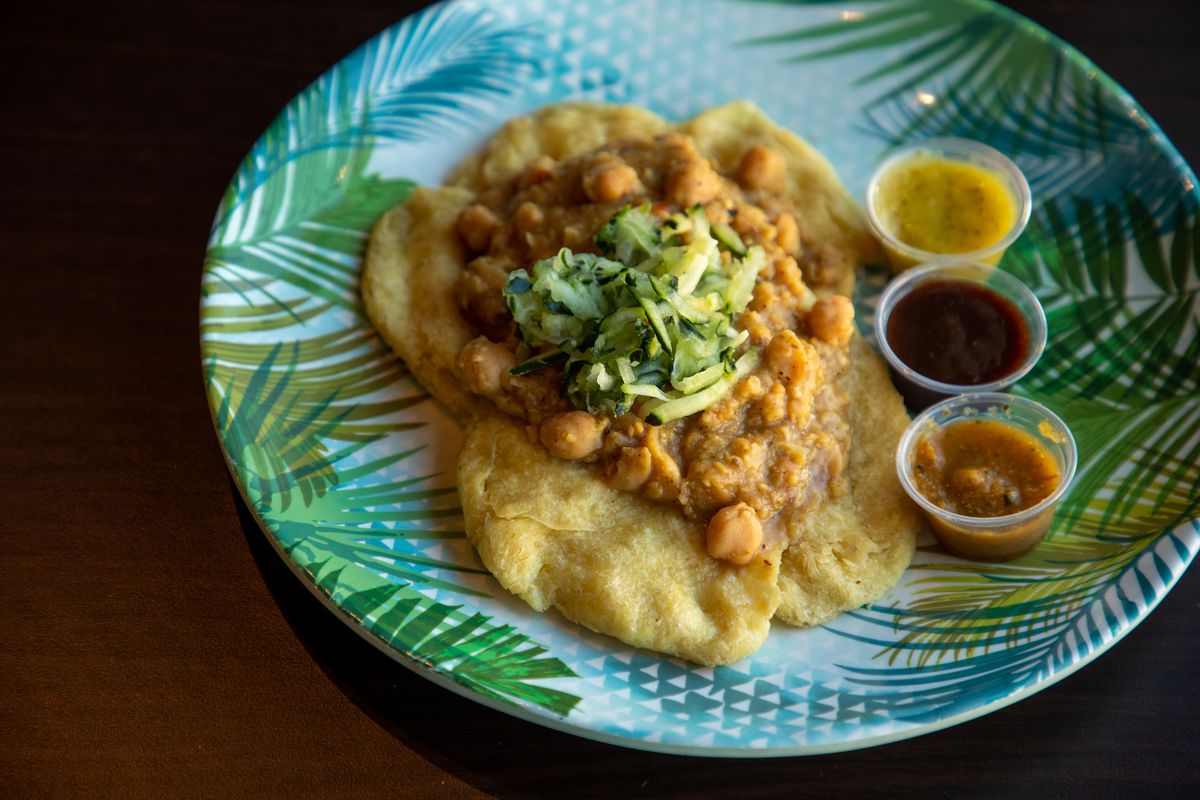 A plate of fried flatbreads topped with a curried chickpea filling next to three sauces.