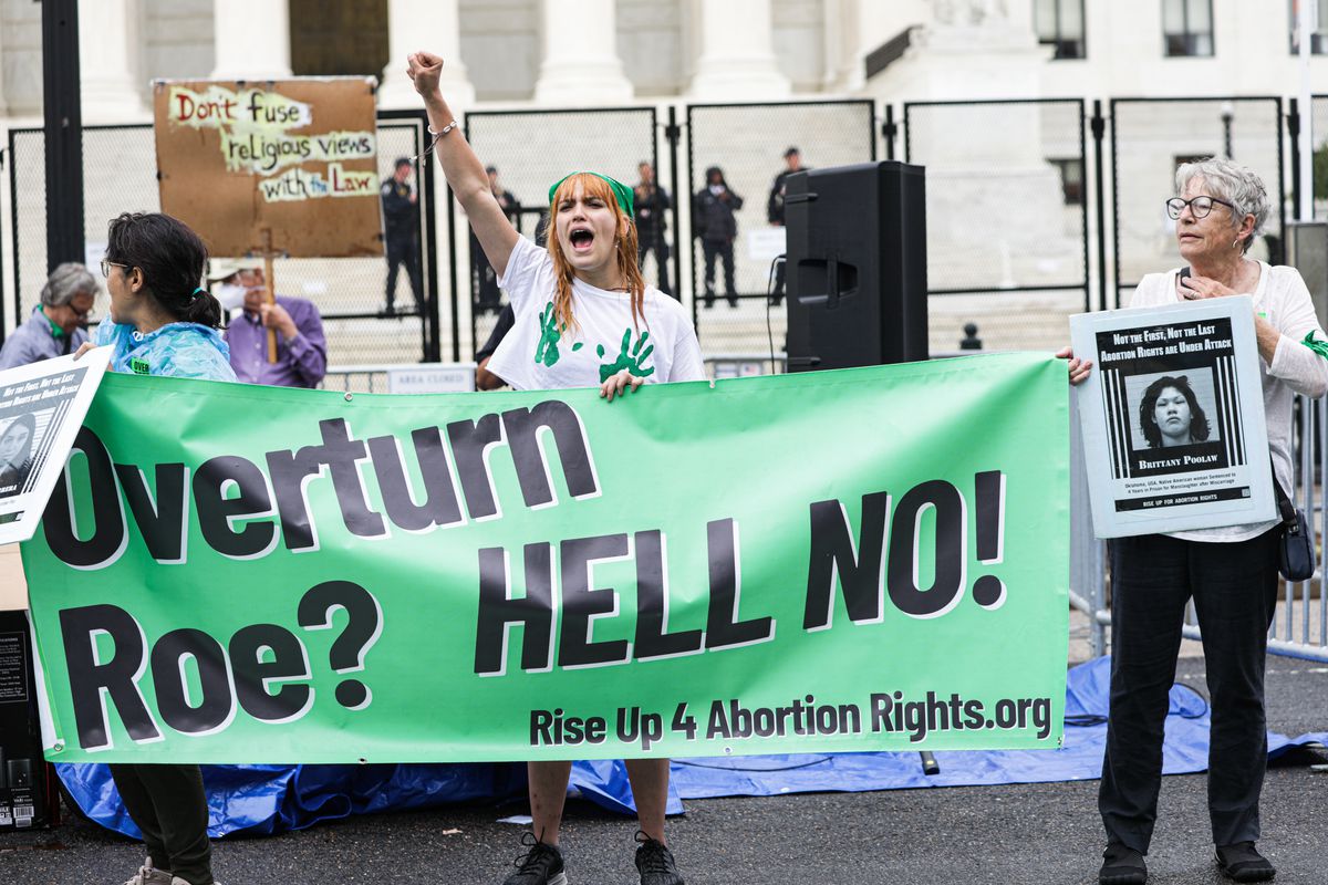Women hold a protest banner outside the Supreme Court that reads, “Overturn Roe? Hell no!”