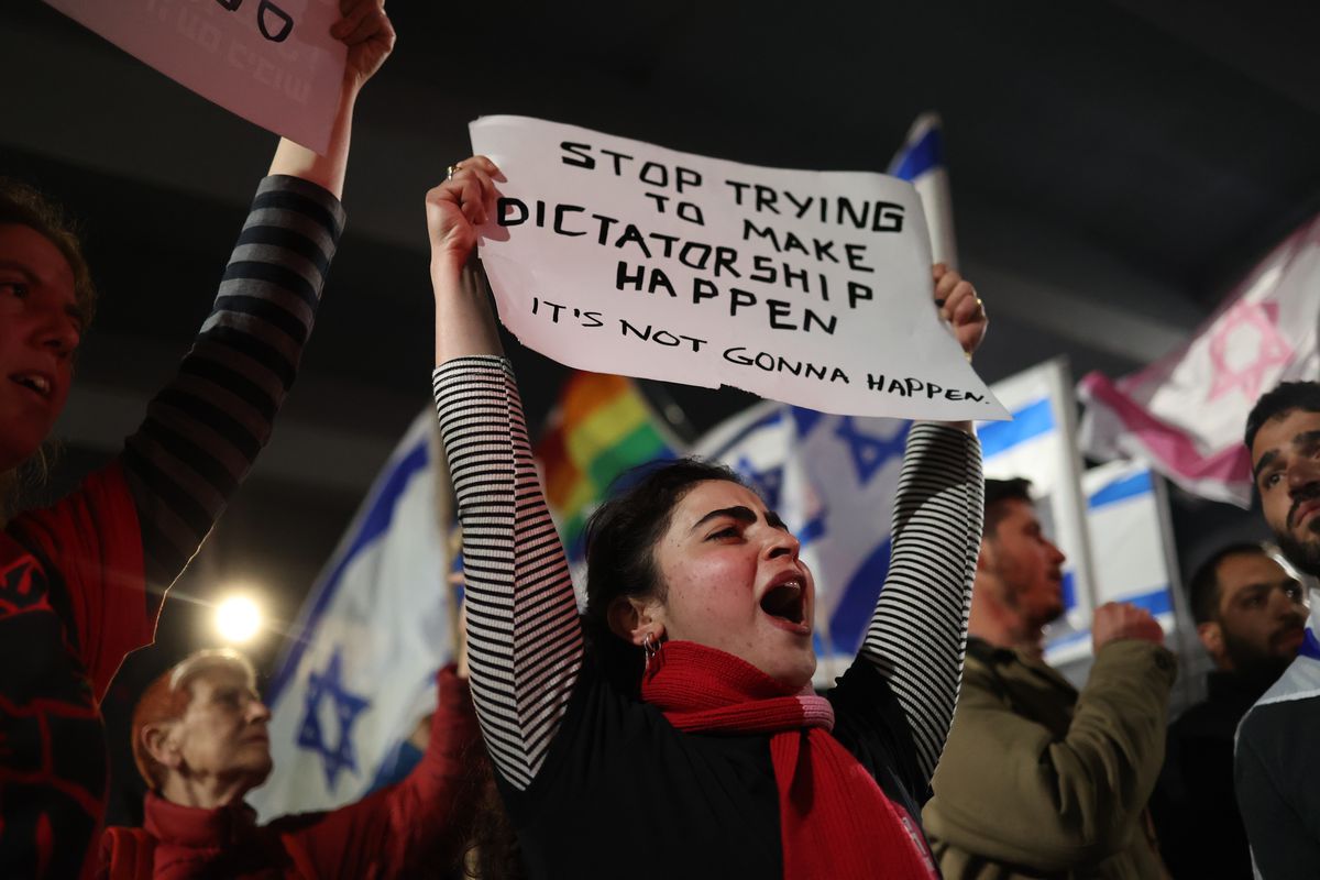 A protester in a crowd holds a sign above her head that reads, “Stop trying to make dictatorship happen. It’s not gonna happen.”
